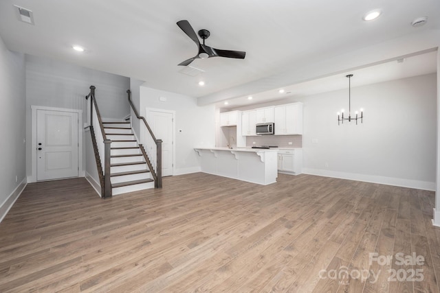 unfurnished living room with ceiling fan with notable chandelier and light wood-type flooring