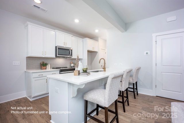 kitchen with appliances with stainless steel finishes, white cabinetry, a breakfast bar area, decorative backsplash, and a kitchen island with sink