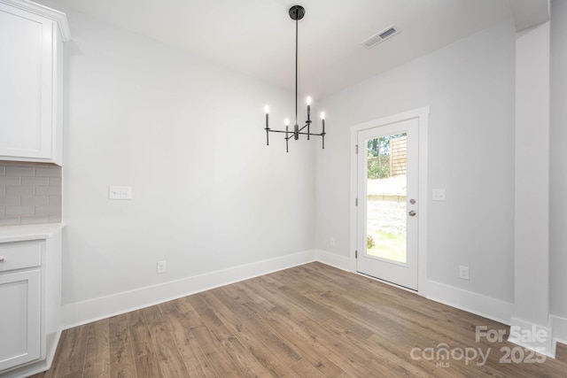 unfurnished dining area featuring an inviting chandelier and light hardwood / wood-style floors