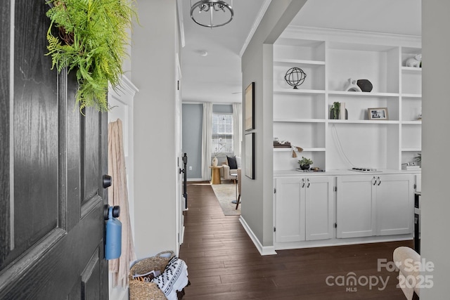 corridor with built in features, baseboards, dark wood-type flooring, and ornamental molding