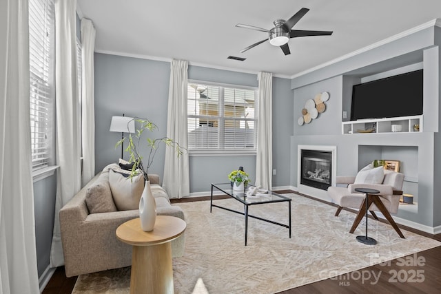 living area with built in features, a ceiling fan, wood finished floors, visible vents, and crown molding