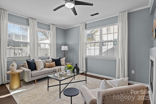 living room with a wealth of natural light, ornamental molding, a ceiling fan, and wood finished floors