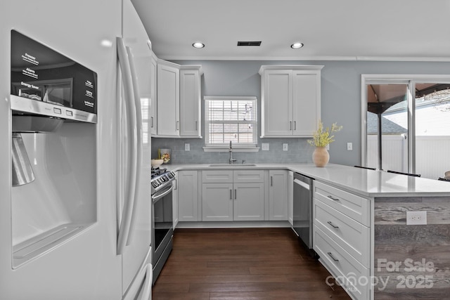 kitchen with a sink, stainless steel appliances, a peninsula, and white cabinetry