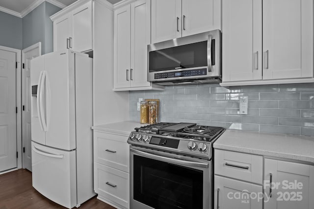 kitchen with dark wood-style flooring, ornamental molding, stainless steel appliances, white cabinets, and backsplash