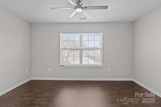 spare room with dark wood finished floors, baseboards, visible vents, and ceiling fan