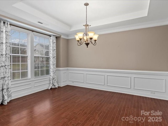 spare room featuring a raised ceiling, ornamental molding, dark wood-type flooring, and a notable chandelier