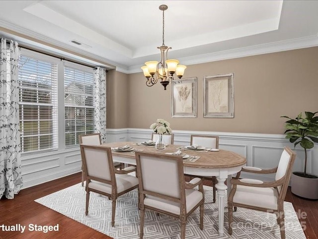 dining room featuring an inviting chandelier, dark wood-type flooring, ornamental molding, and a raised ceiling