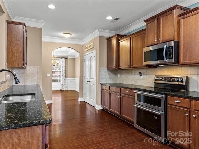 kitchen featuring sink, dark stone countertops, ornamental molding, stainless steel appliances, and dark wood-type flooring