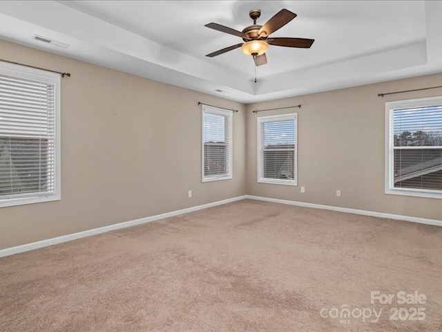 carpeted empty room featuring a raised ceiling, plenty of natural light, and ceiling fan