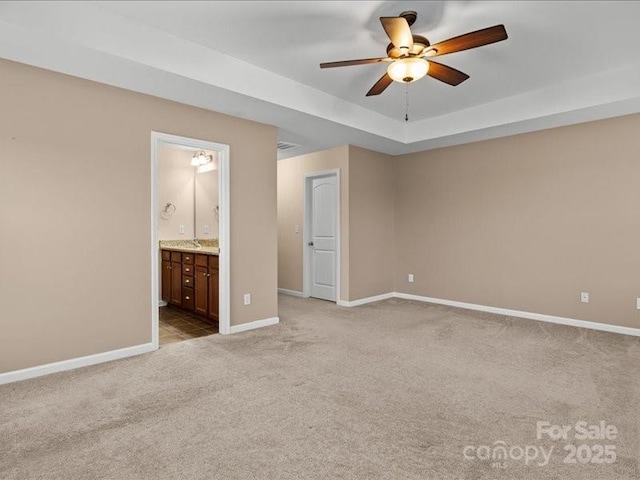 unfurnished bedroom with light carpet, ensuite bath, a raised ceiling, and ceiling fan