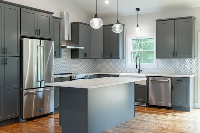 kitchen with light wood finished floors, gray cabinetry, wall chimney range hood, appliances with stainless steel finishes, and a sink