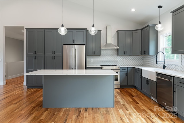 kitchen featuring wall chimney exhaust hood, wood finished floors, gray cabinets, and appliances with stainless steel finishes