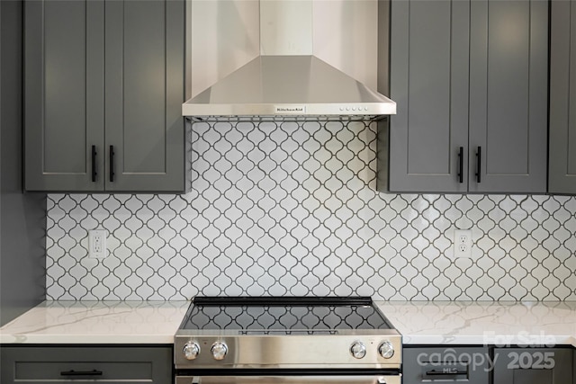 kitchen featuring light stone countertops, stove, and wall chimney range hood