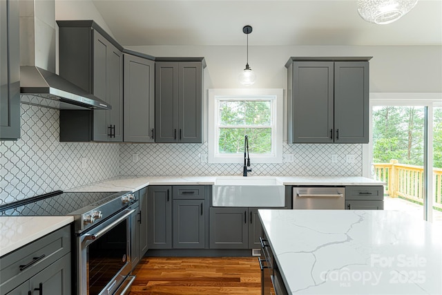 kitchen with gray cabinets, appliances with stainless steel finishes, wall chimney range hood, and a sink