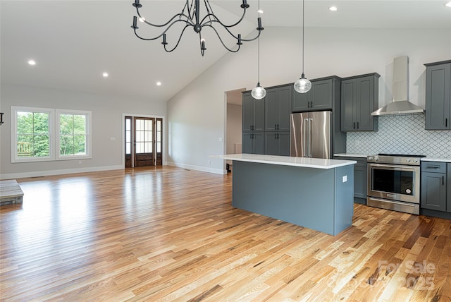 kitchen featuring gray cabinets, light countertops, appliances with stainless steel finishes, wall chimney exhaust hood, and a center island