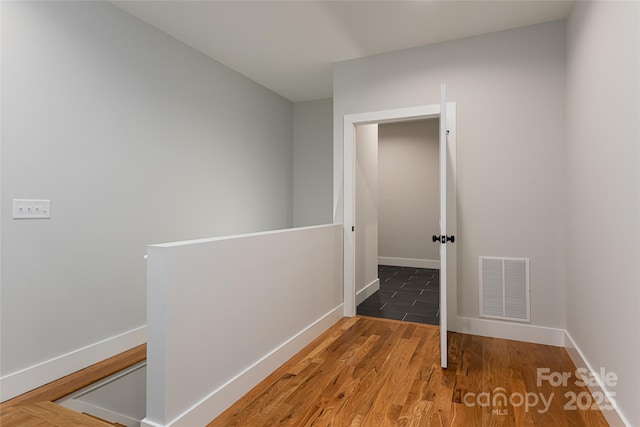hall featuring an upstairs landing, wood finished floors, visible vents, and baseboards