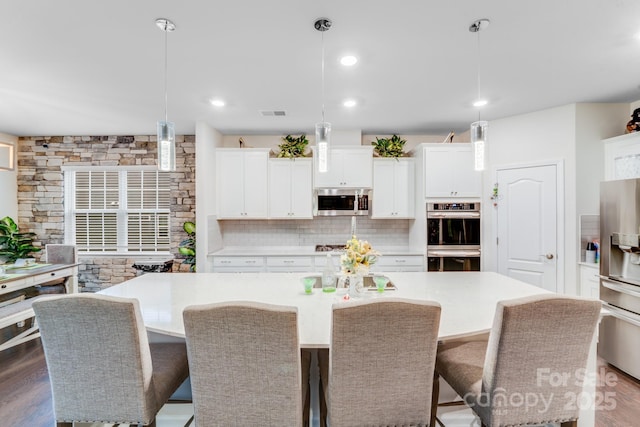 kitchen featuring decorative light fixtures, a breakfast bar area, stainless steel appliances, and a center island with sink