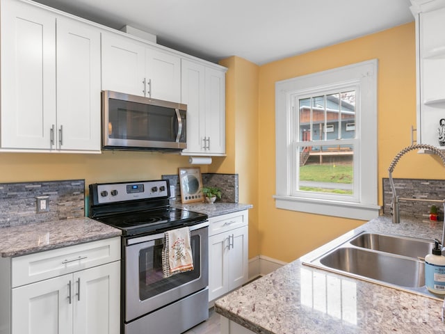 kitchen with light stone counters, a sink, white cabinetry, stainless steel appliances, and baseboards
