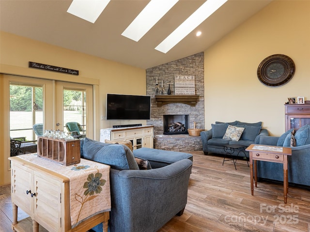 living room with a stone fireplace, high vaulted ceiling, light hardwood / wood-style floors, and a skylight