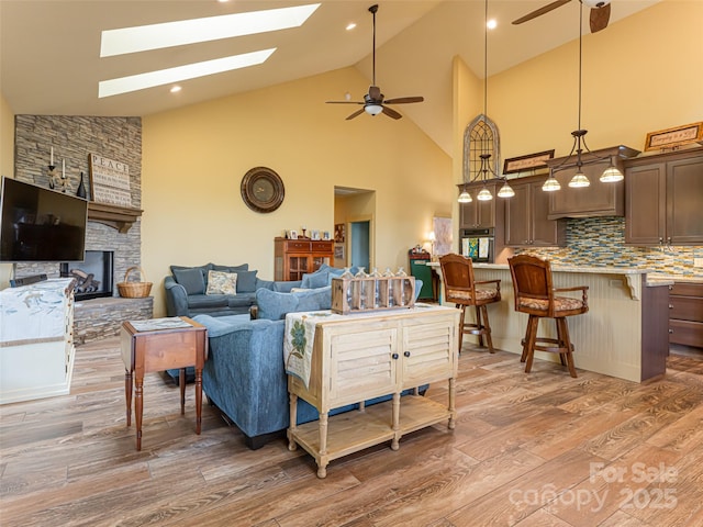 living room with high vaulted ceiling, a fireplace, a skylight, hardwood / wood-style flooring, and ceiling fan