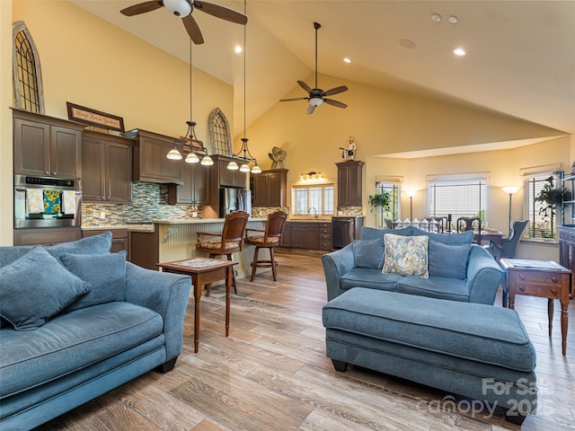 living room with sink, high vaulted ceiling, ceiling fan, and light wood-type flooring