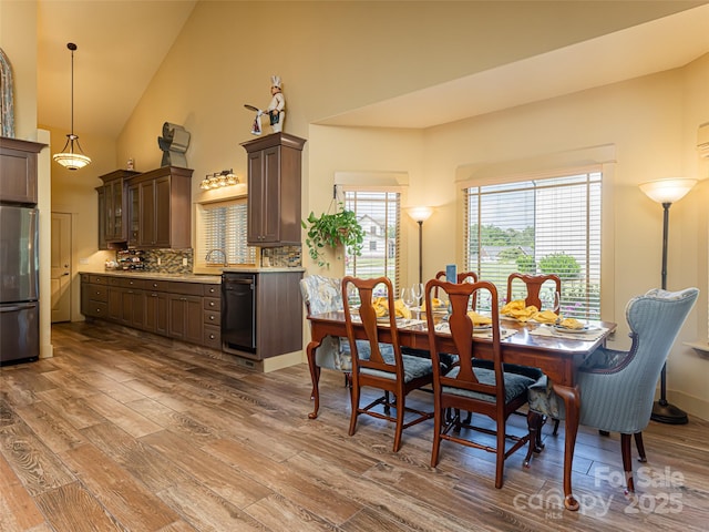 dining space with sink, wood-type flooring, and high vaulted ceiling