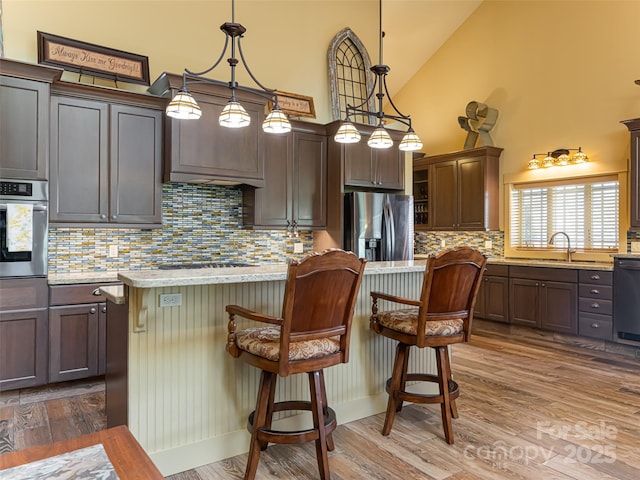 kitchen featuring pendant lighting, a breakfast bar area, a center island, dark brown cabinetry, and black appliances