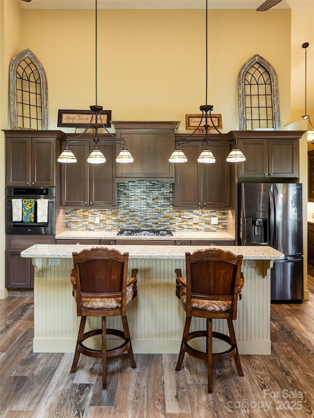 kitchen with a breakfast bar area, dark brown cabinets, hanging light fixtures, appliances with stainless steel finishes, and an island with sink