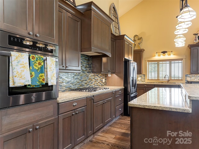 kitchen featuring tasteful backsplash, light stone counters, vaulted ceiling, pendant lighting, and stainless steel appliances