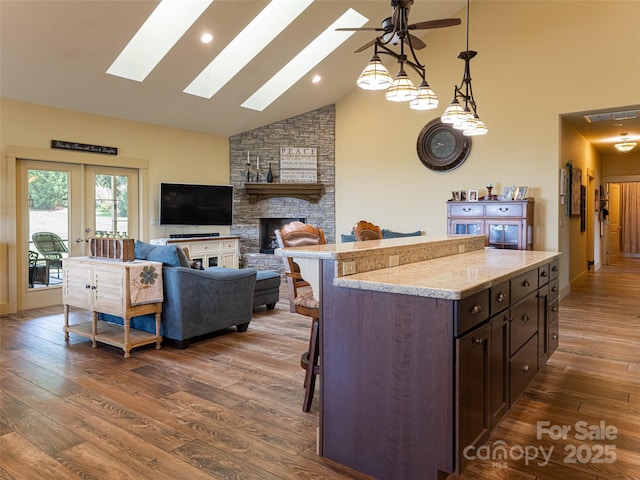 kitchen with dark wood-type flooring, a breakfast bar area, dark brown cabinets, pendant lighting, and a fireplace