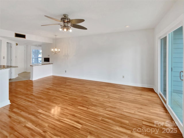 unfurnished living room with ceiling fan with notable chandelier and light hardwood / wood-style flooring