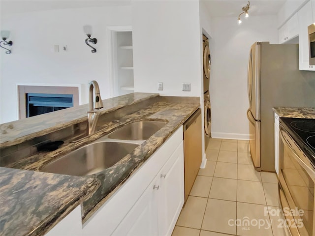 kitchen with stacked washer and dryer, sink, stainless steel appliances, white cabinets, and dark stone counters