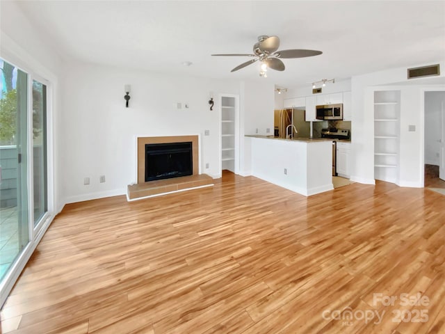 unfurnished living room with built in features, ceiling fan, and light wood-type flooring