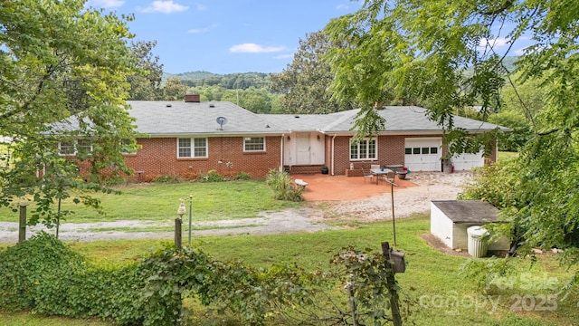 rear view of property featuring a patio, a shed, a lawn, and a garage