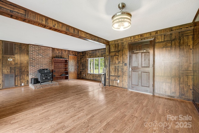 unfurnished living room featuring wooden walls, light hardwood / wood-style floors, and a wood stove