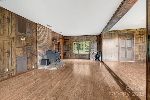 unfurnished living room with hardwood / wood-style floors, wooden walls, and a wood stove