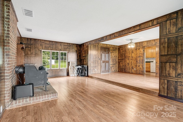 unfurnished living room with a wood stove, a textured ceiling, light hardwood / wood-style floors, and wood walls