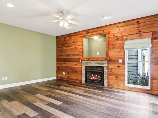 unfurnished living room with hardwood / wood-style floors, a stone fireplace, wooden walls, and ceiling fan