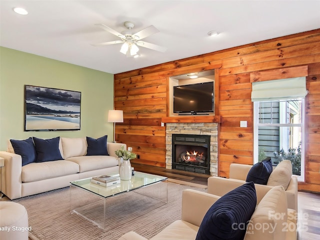 living room featuring ceiling fan, wooden walls, a fireplace, and light wood-type flooring