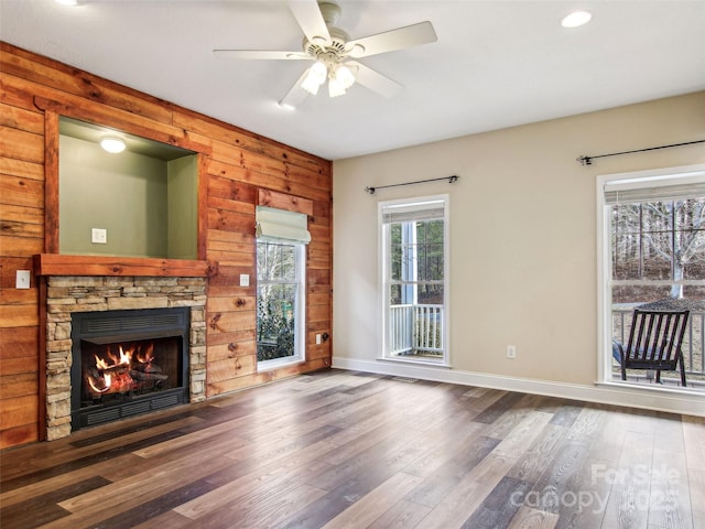 unfurnished living room featuring ceiling fan, dark wood-type flooring, wooden walls, and a fireplace