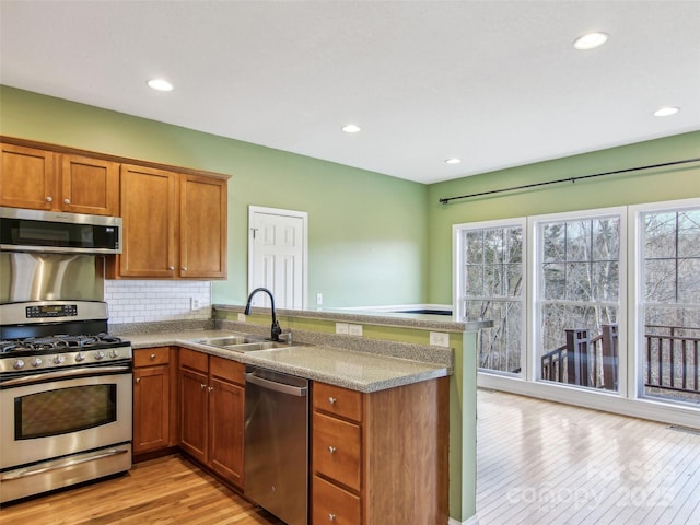 kitchen with sink, tasteful backsplash, light wood-type flooring, kitchen peninsula, and stainless steel appliances