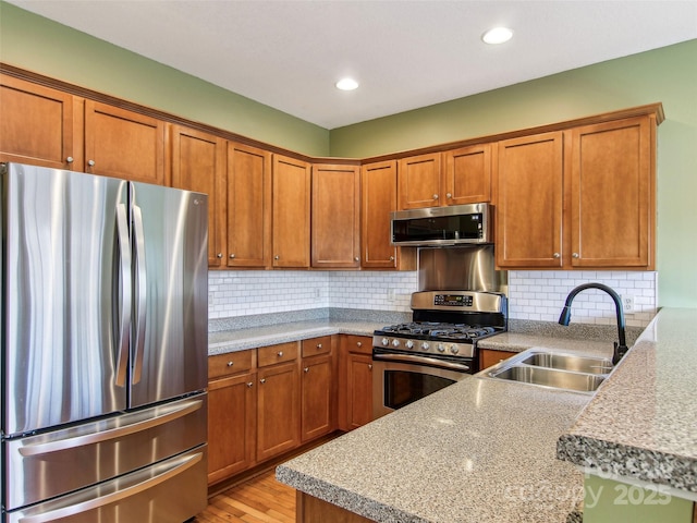 kitchen featuring appliances with stainless steel finishes, sink, decorative backsplash, light stone countertops, and light wood-type flooring