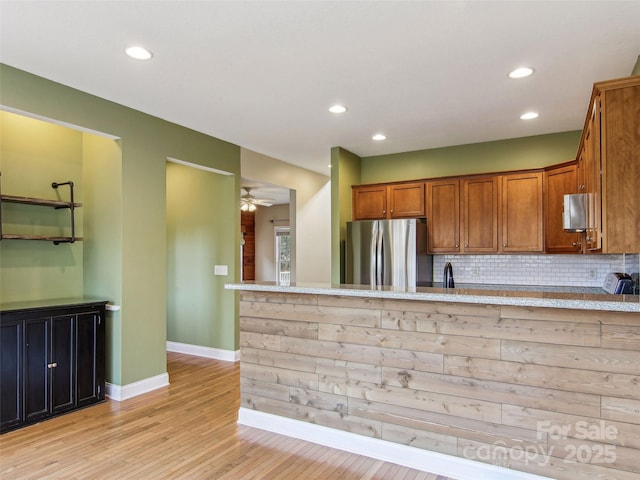 kitchen with tasteful backsplash, light hardwood / wood-style flooring, stainless steel fridge, kitchen peninsula, and light stone countertops