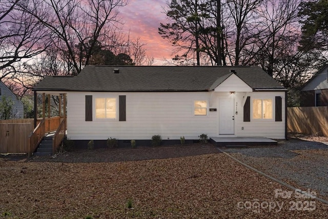 view of front of property with a patio area, a shingled roof, and fence