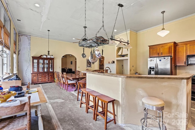 kitchen with concrete flooring, pendant lighting, a breakfast bar area, stainless steel fridge with ice dispenser, and crown molding