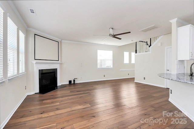 unfurnished living room with dark wood-type flooring, ceiling fan, plenty of natural light, and crown molding