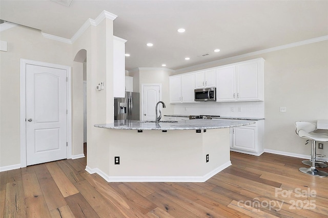 kitchen with sink, light hardwood / wood-style flooring, stainless steel appliances, light stone countertops, and white cabinets