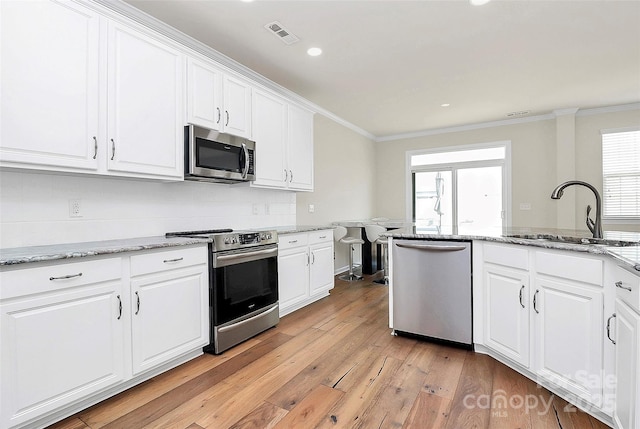 kitchen with white cabinetry, sink, stainless steel appliances, crown molding, and light stone countertops