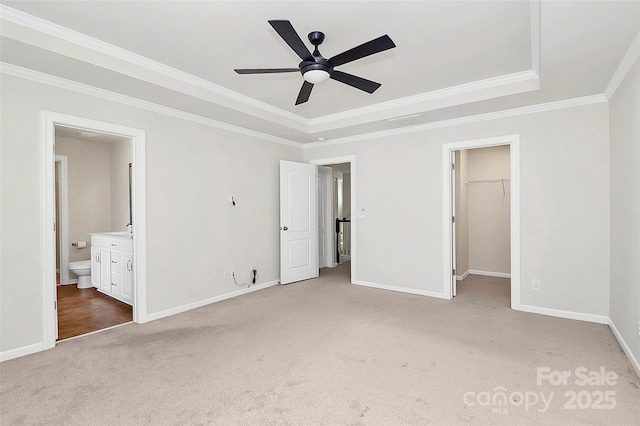 unfurnished bedroom with crown molding, connected bathroom, a tray ceiling, light carpet, and a spacious closet