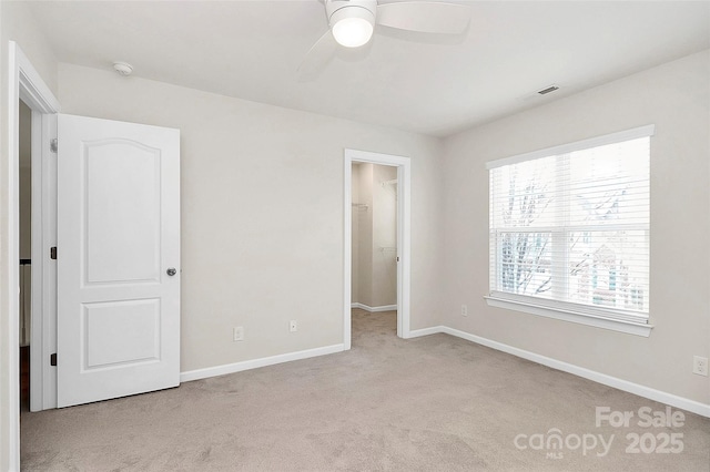 unfurnished bedroom with ceiling fan, a closet, a spacious closet, and light carpet